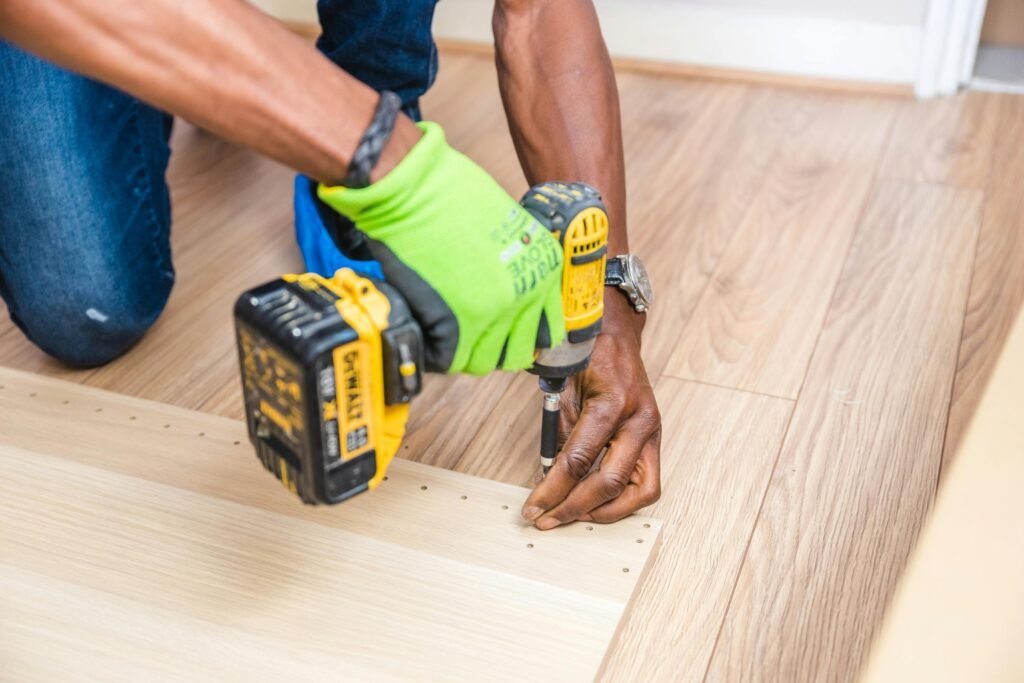 pexels-photo-1249610-1249610 Close-up of handyman drilling wood indoors with green gloves and cordless drill.